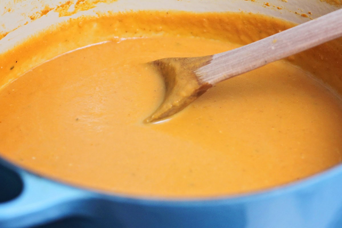 A wooden spoon in a pot of pumpkin soup.