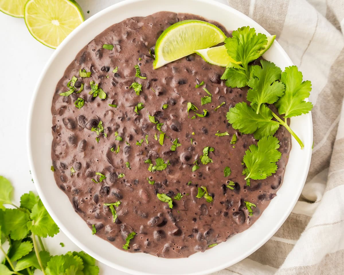 Refried black beans served in a white bowl with lime and cilantro.