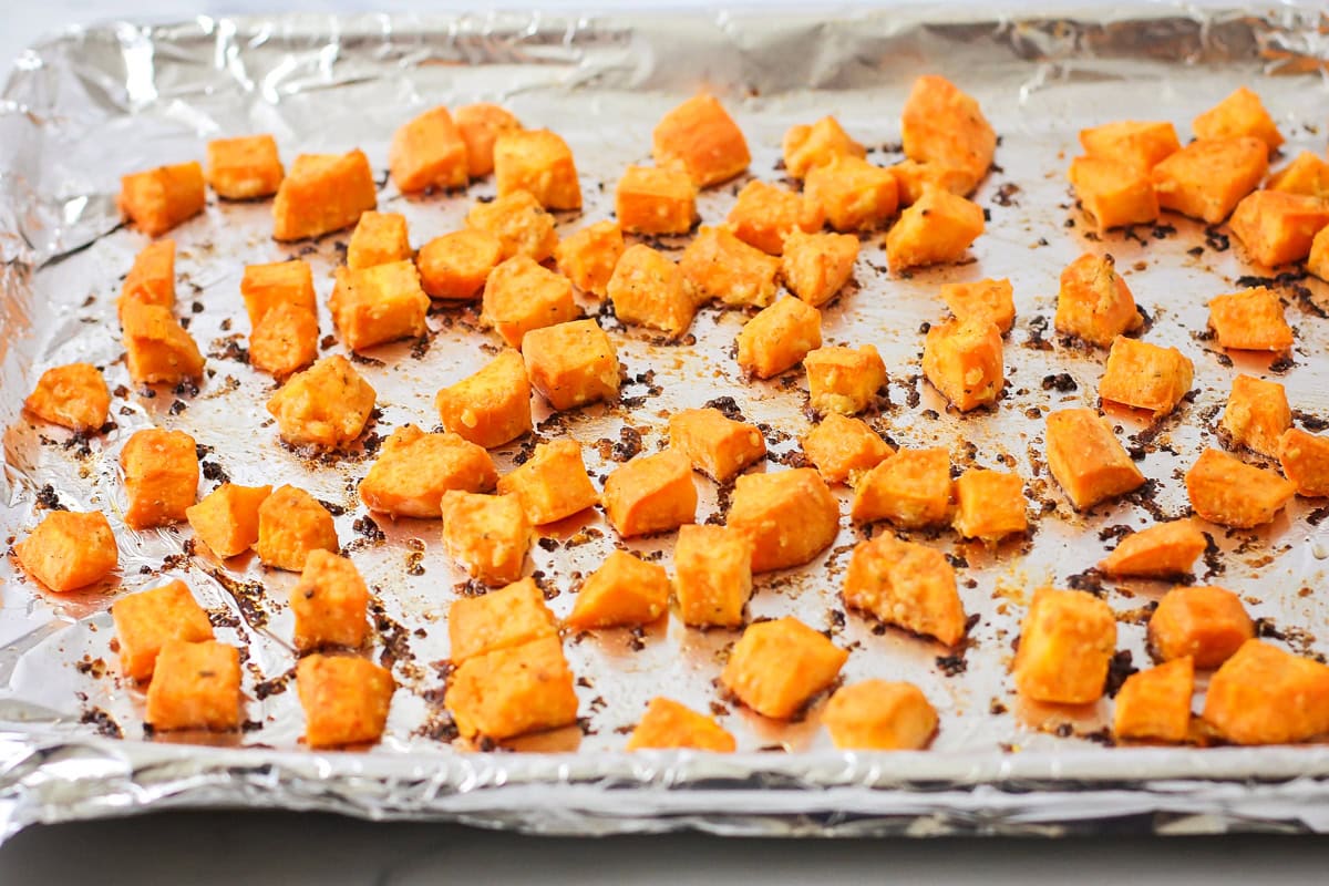 Baked sweet potato cubes on foil lined baking sheet fresh from oven.