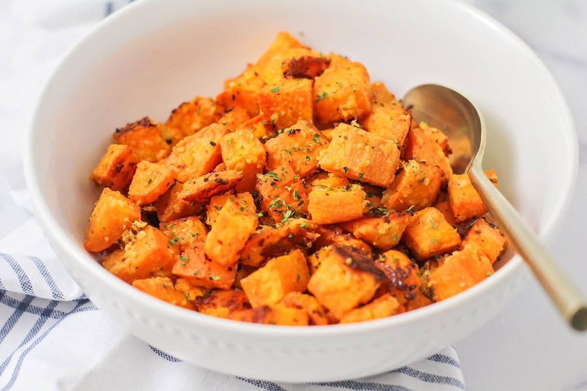 Roasted sweet potato cubes in white glass bowl with gold spoon.