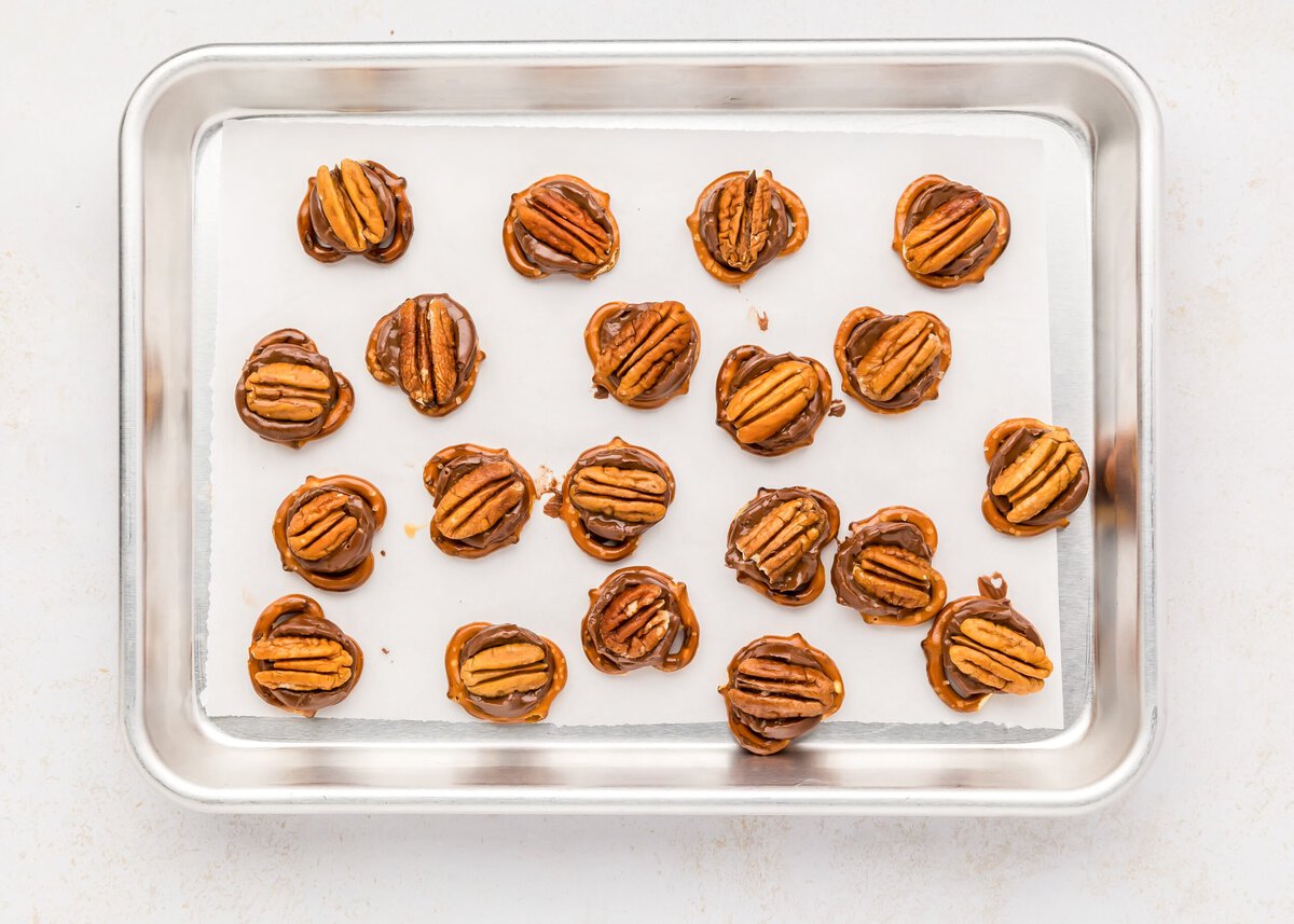 Pressing pecan halves onto melted Rolos on a lined baking sheet.