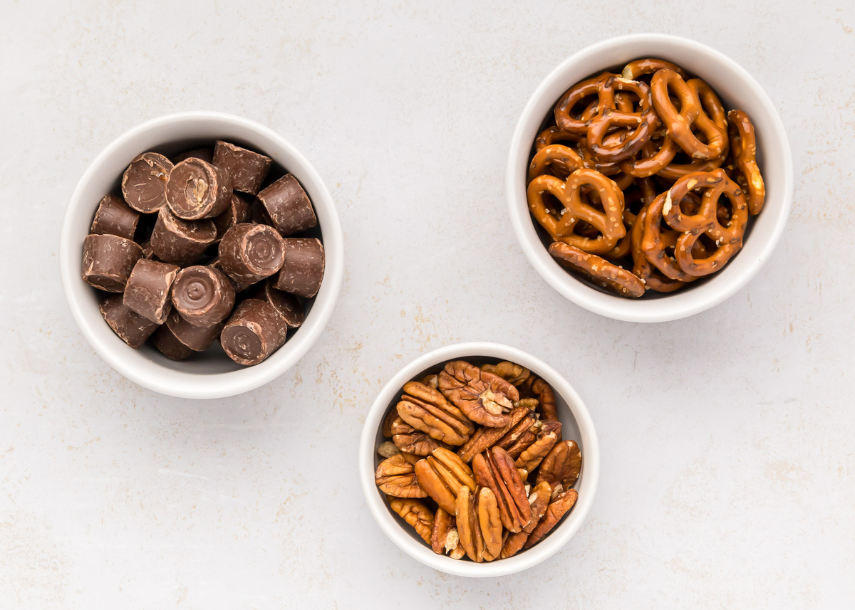 3 bowl of rolos, pretzels, and pecans on a kitchen counter.