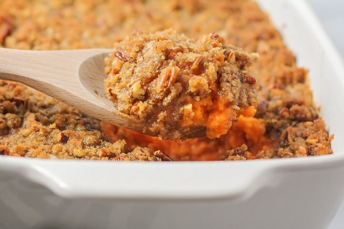 Scooping sweet potato souffle from a white baking dish.