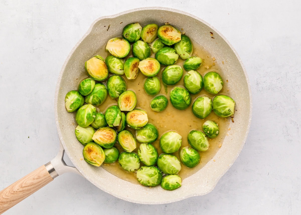 Halved Brussels sprouts cooking in broth in a skillet.