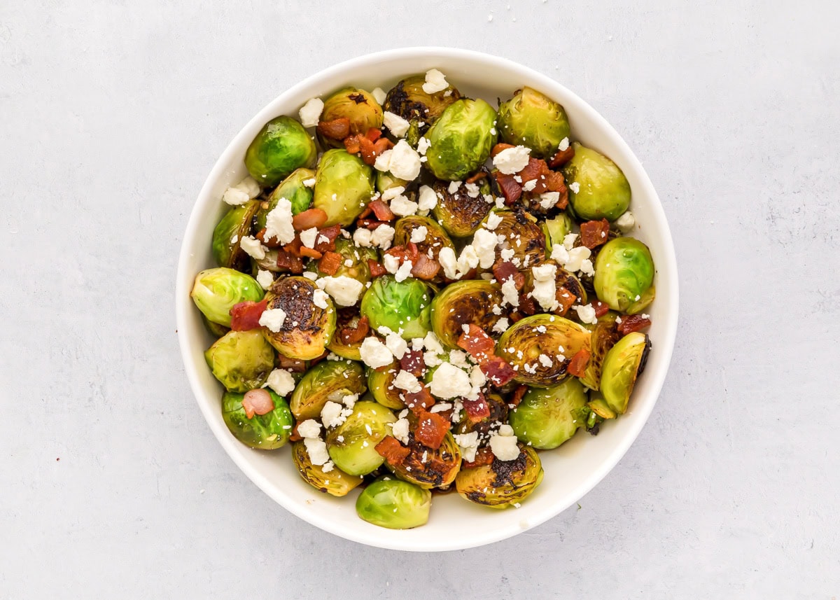 Bacon and feta crumbles on top of Brussels sprouts in a skillet.