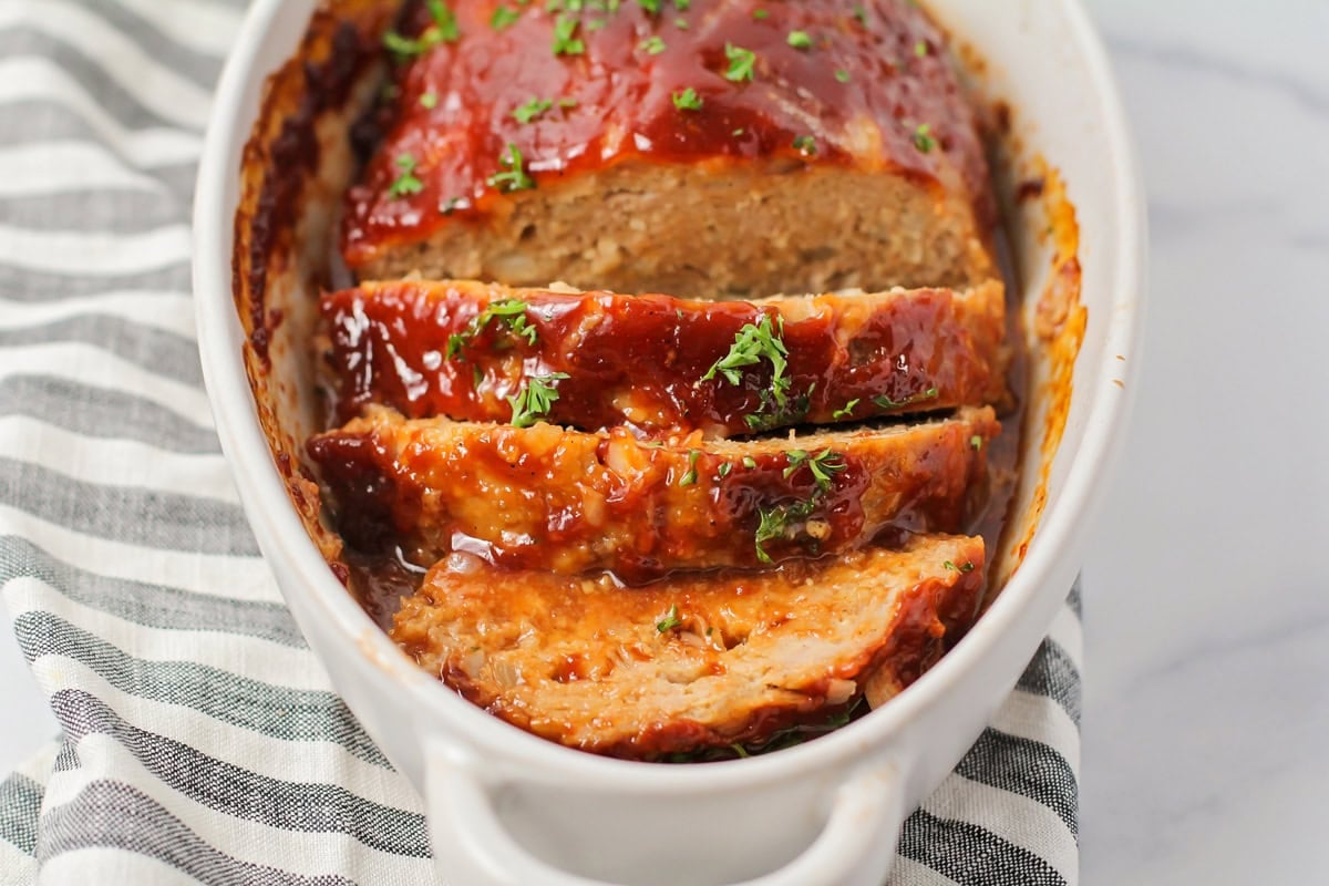 Cooked and sliced meatloaf in a white baking dish.