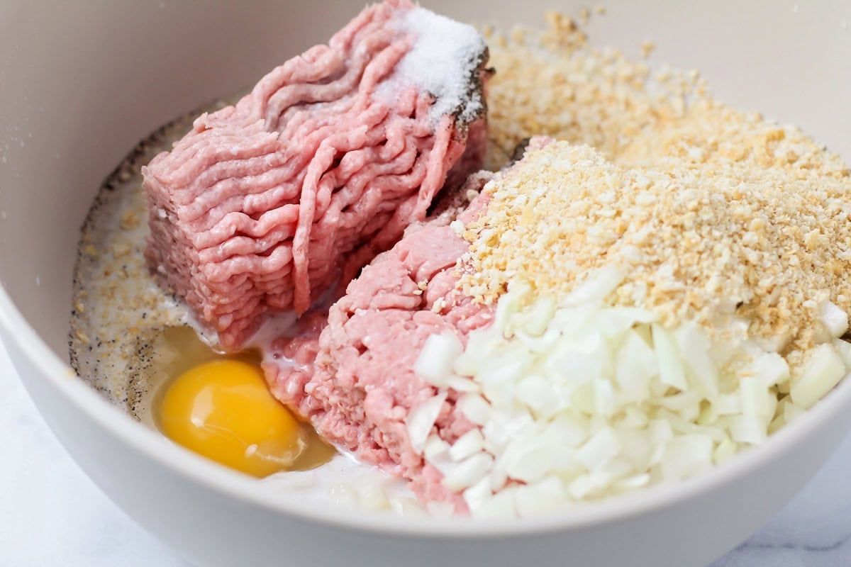 Ground turkey, diced onion, an egg, and crumbs in a white bowl.