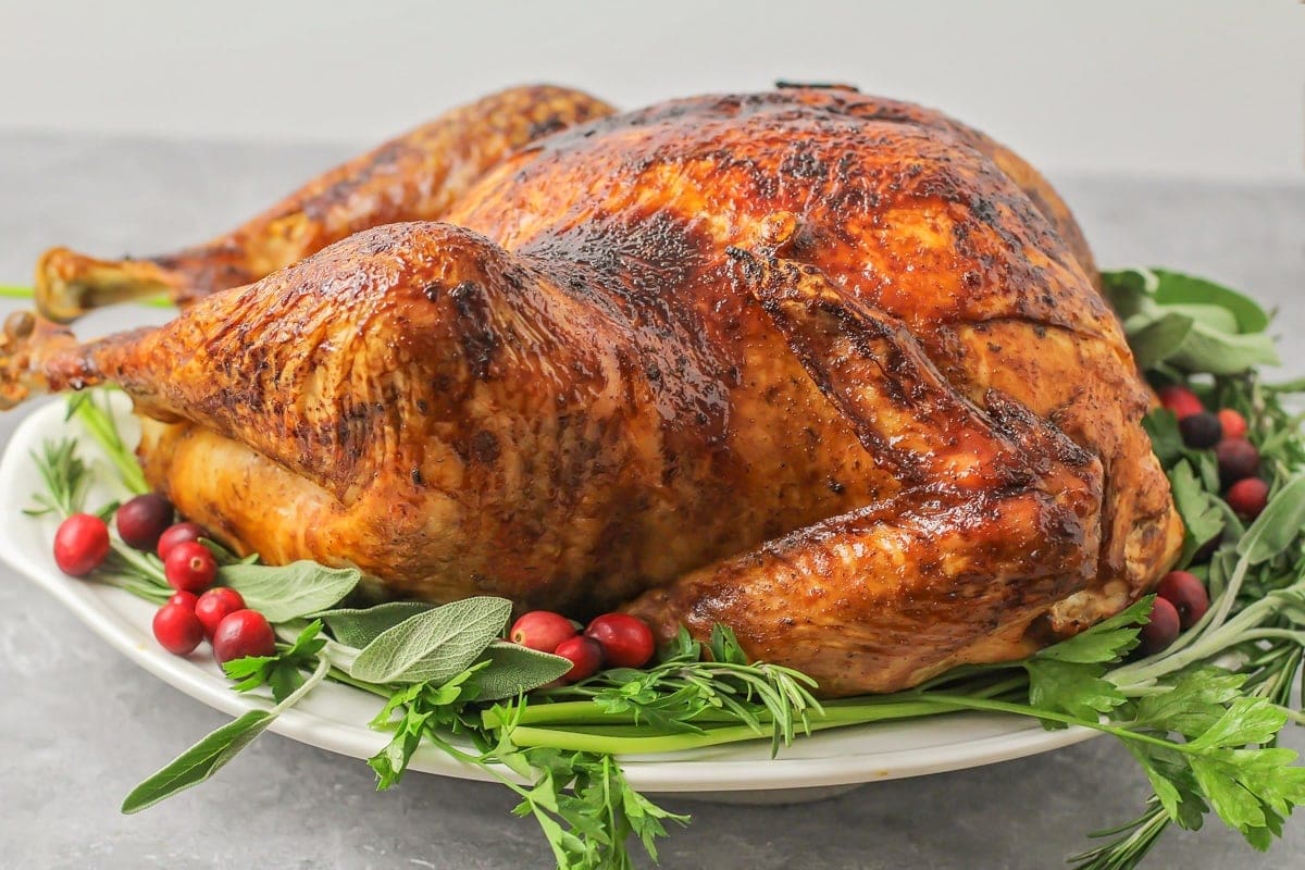 A roasted turkey on a bed of greens with fresh cranberries to garnish. 