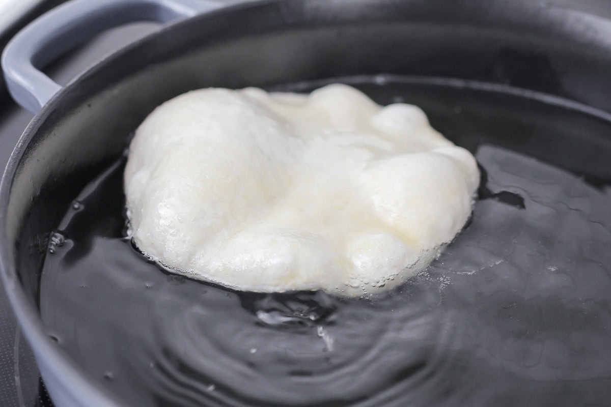 A flatten dough ball frying in a pan of oil.