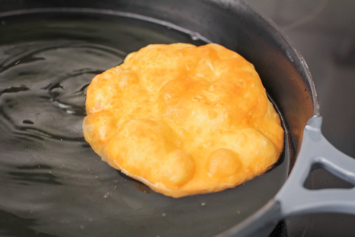 A disc of dough frying in a pan of oil.