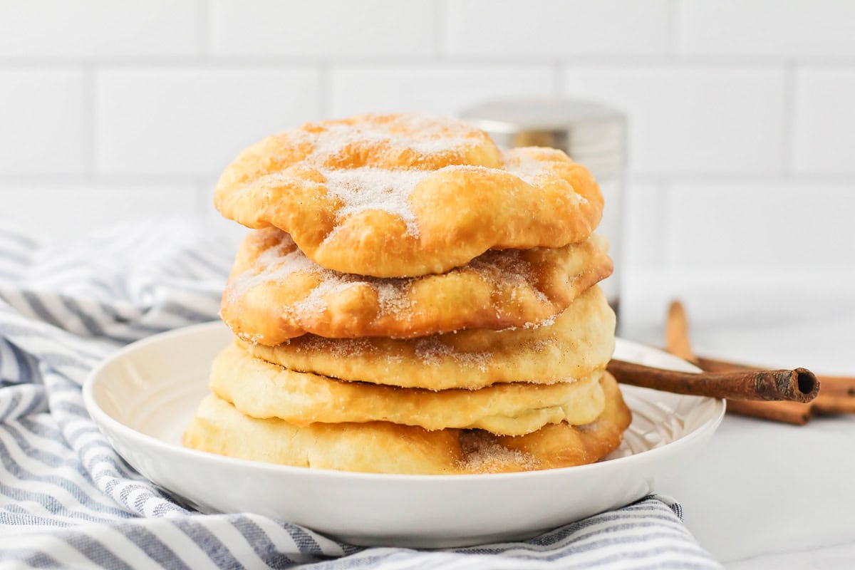 Bunuelos stacked on a white plate and covered in cinnamon and sugar.