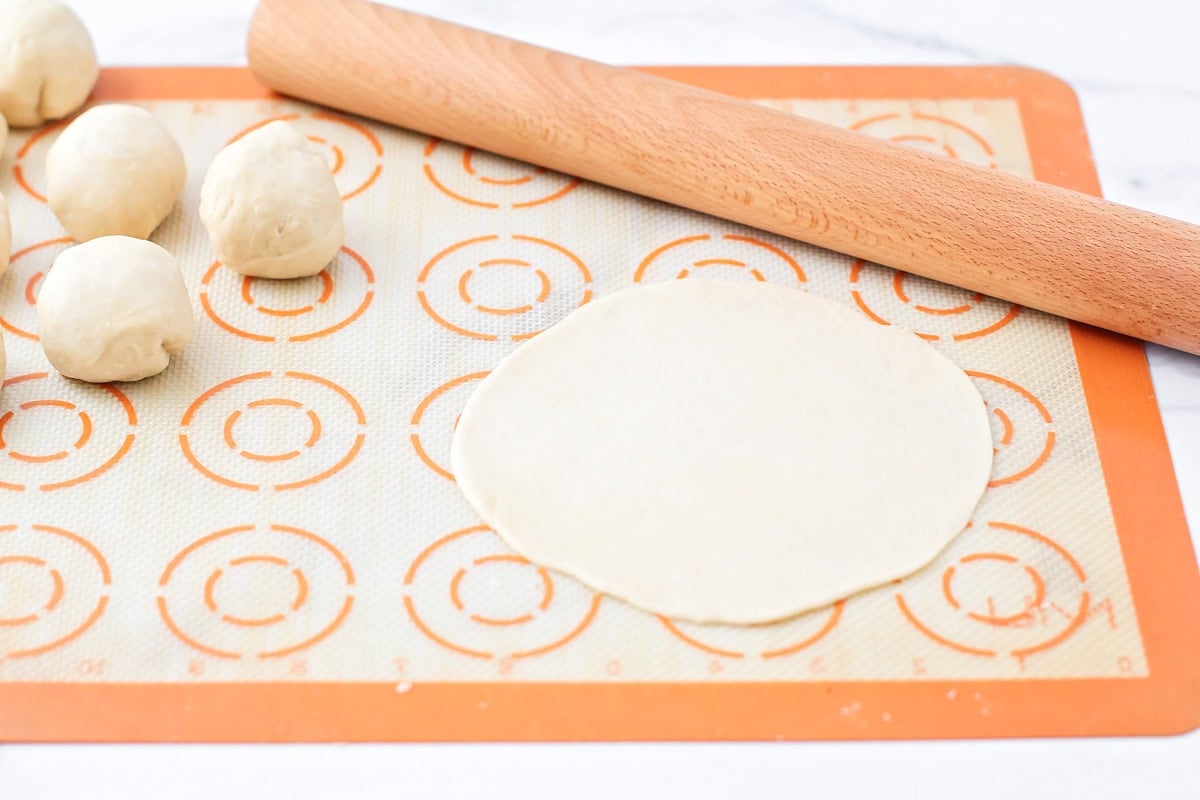 Dough balls being rolled out on a silpat mat.