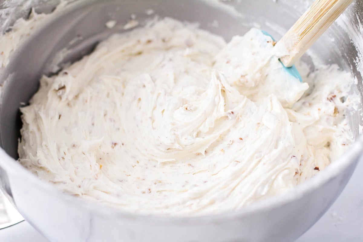 Mixing frosting in a bowl with chopped pecans.