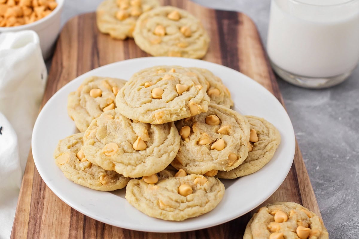 Butterscotch cookies stacked on white plate with glass of milk.