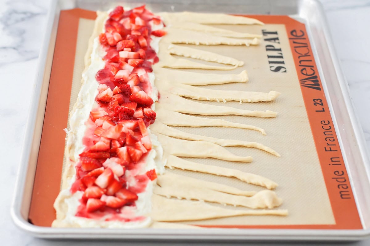 Adding cream cheese mixture, jam, and fresh strawberries to the crescent rolls.