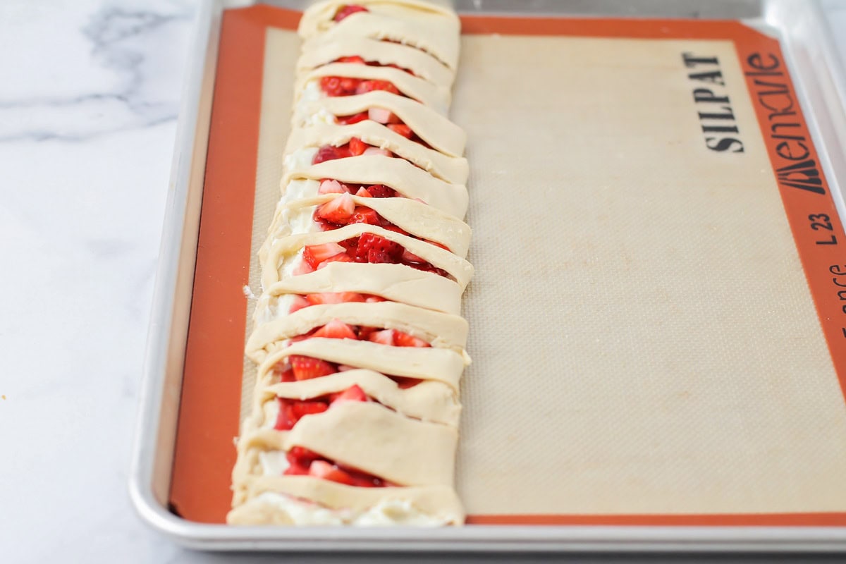 Folding the crescent roll strips over the filling.