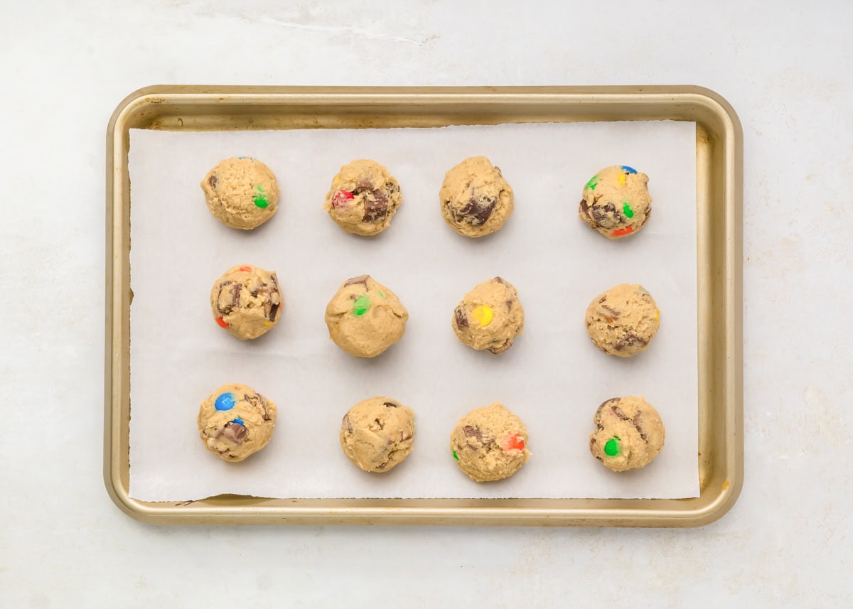 Candy cookie dough balls on parchment paper lined baking sheet.