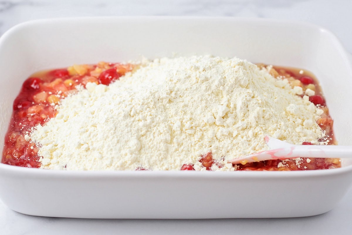 Cake mix poured over cherries and pineapple in baking dish.