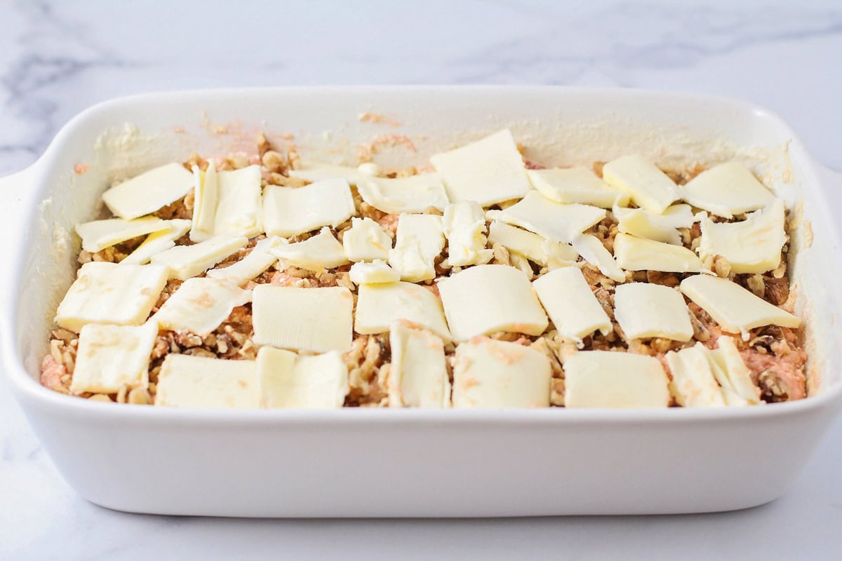 Butter pats over walnuts and cherry dump cake batter in baking dish.