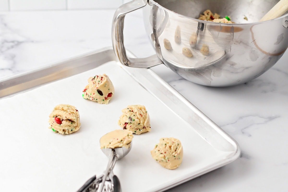 Scooping cookie dough on a lined baking sheet.