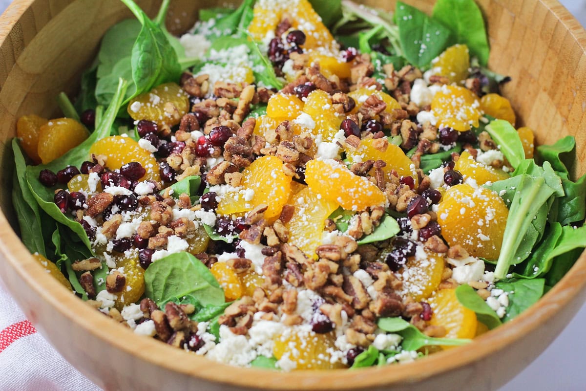 A bed of greens topped with fruit, nuts, and feta.