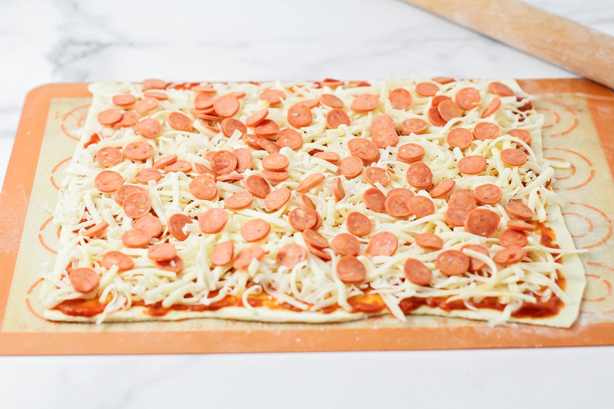 Adding cheese and pepperoni to a puff pastry sheet.