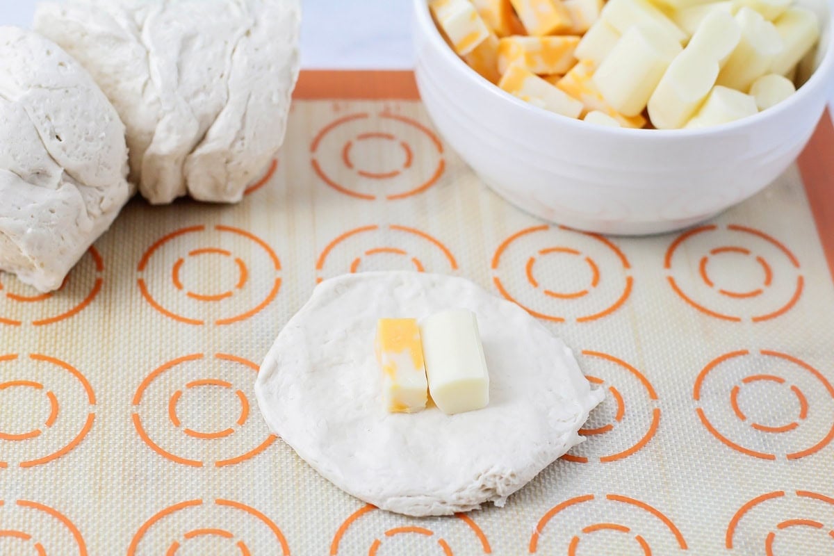 Adding cheese to the center of a biscuit dough.