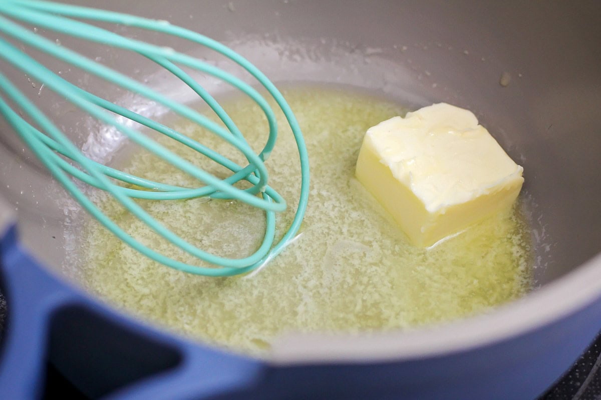 A piece of stick butter in a pot with a whisk stirring it. 