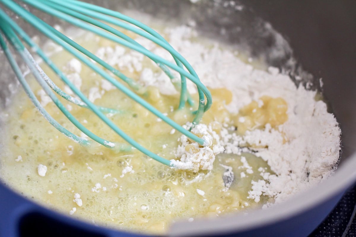 A photo of a whisk mixing a roux in a pot. 