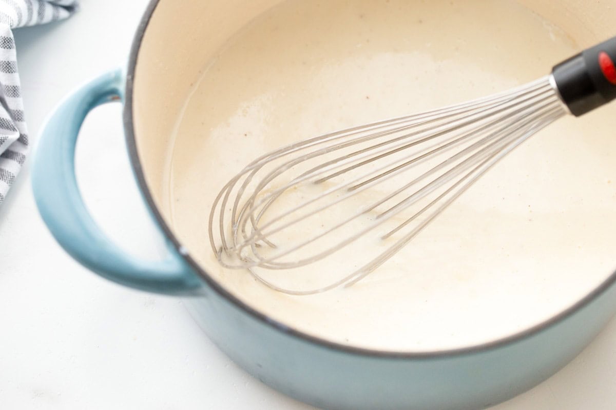 A pot of white liquid with a whisk mixing it. 