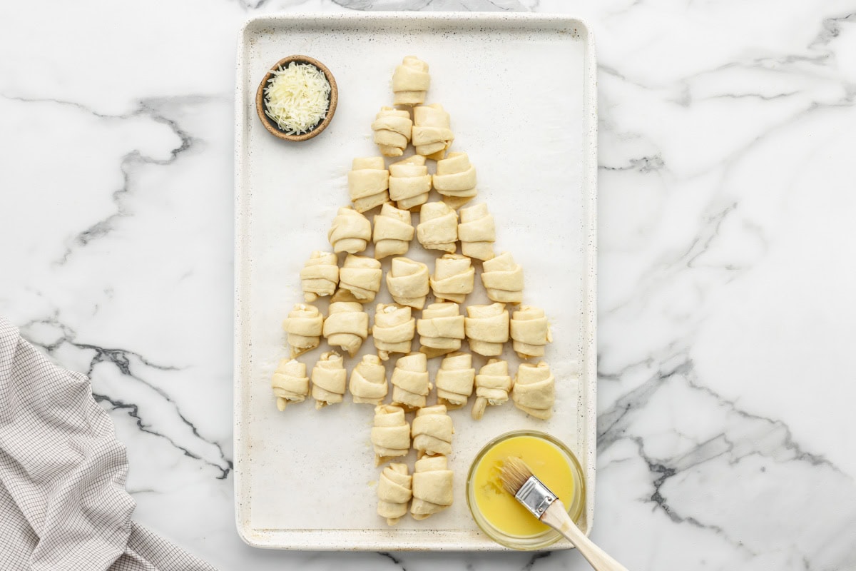 Filled crescent rolls in the shape of a Christmas tree on a lined baking sheet.