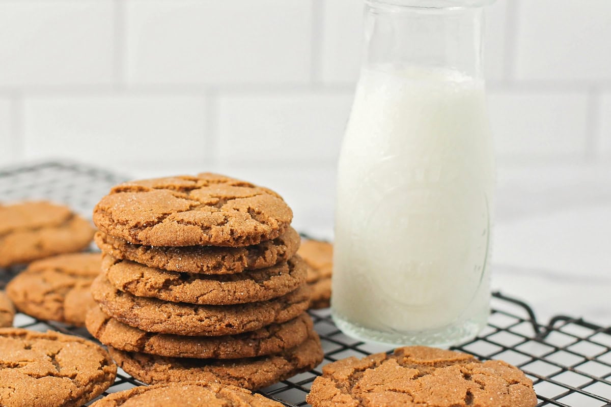Ginger snaps stacked on a wire rack with a glass jar of milk.