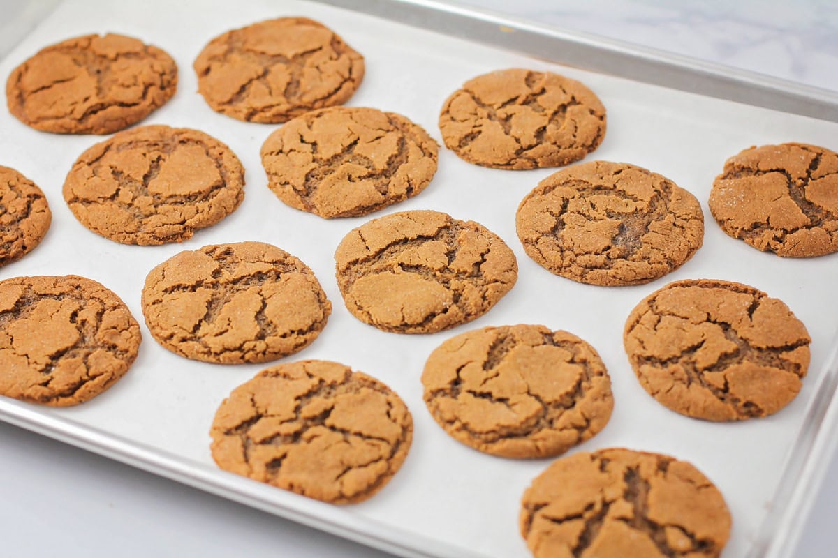 Baked ginger snap cookies on a lined baking sheet.