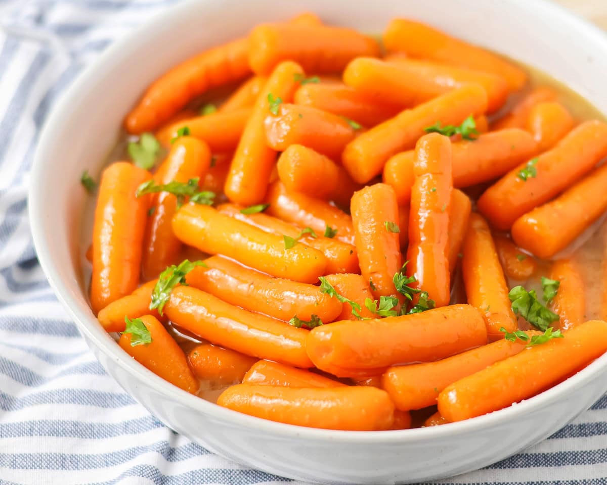 Brown sugar glazed carrots in white bowl with parsley on top.