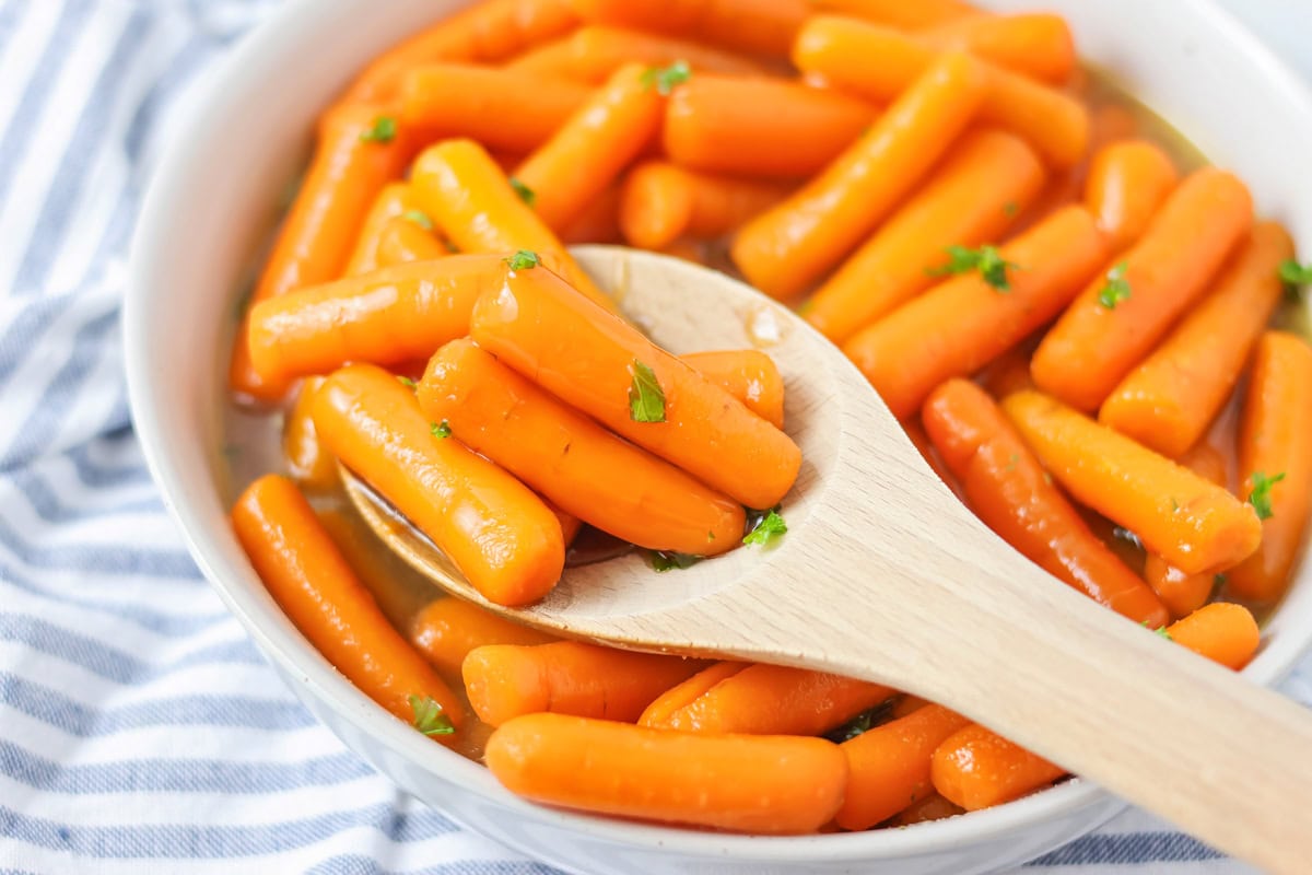 Glazed carrots in white bowl with chopped parsley on top.