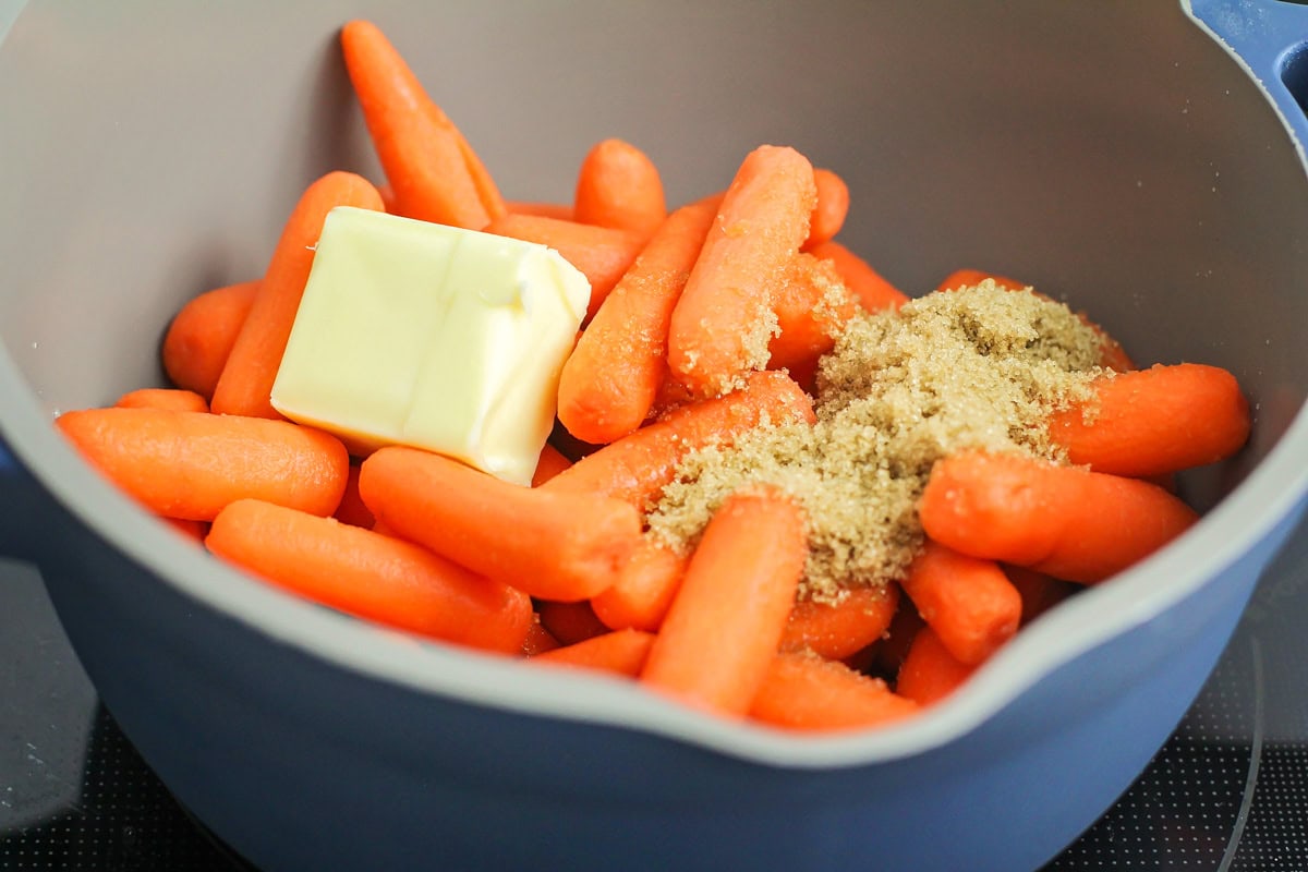 Ingredients for glazed carrots in pot - baby carrots, butter, water and brown sugar.