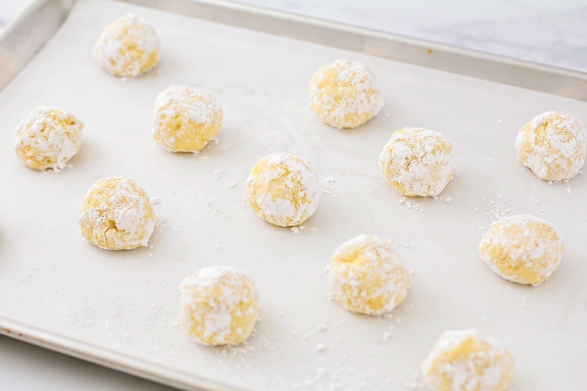 Gooey butter cookie dough balls on parchment paper lined cookie sheet.