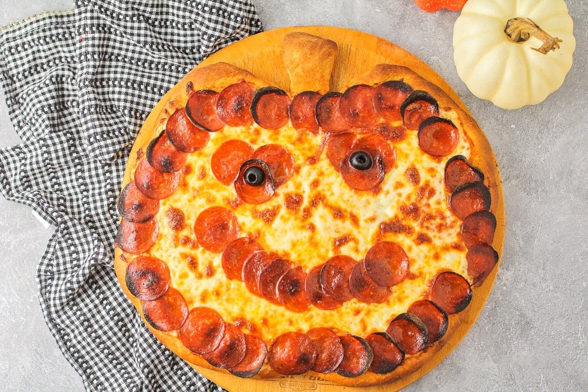 A cooked pumpkin shaped pizza decorated with pepperonis to look like a face. 