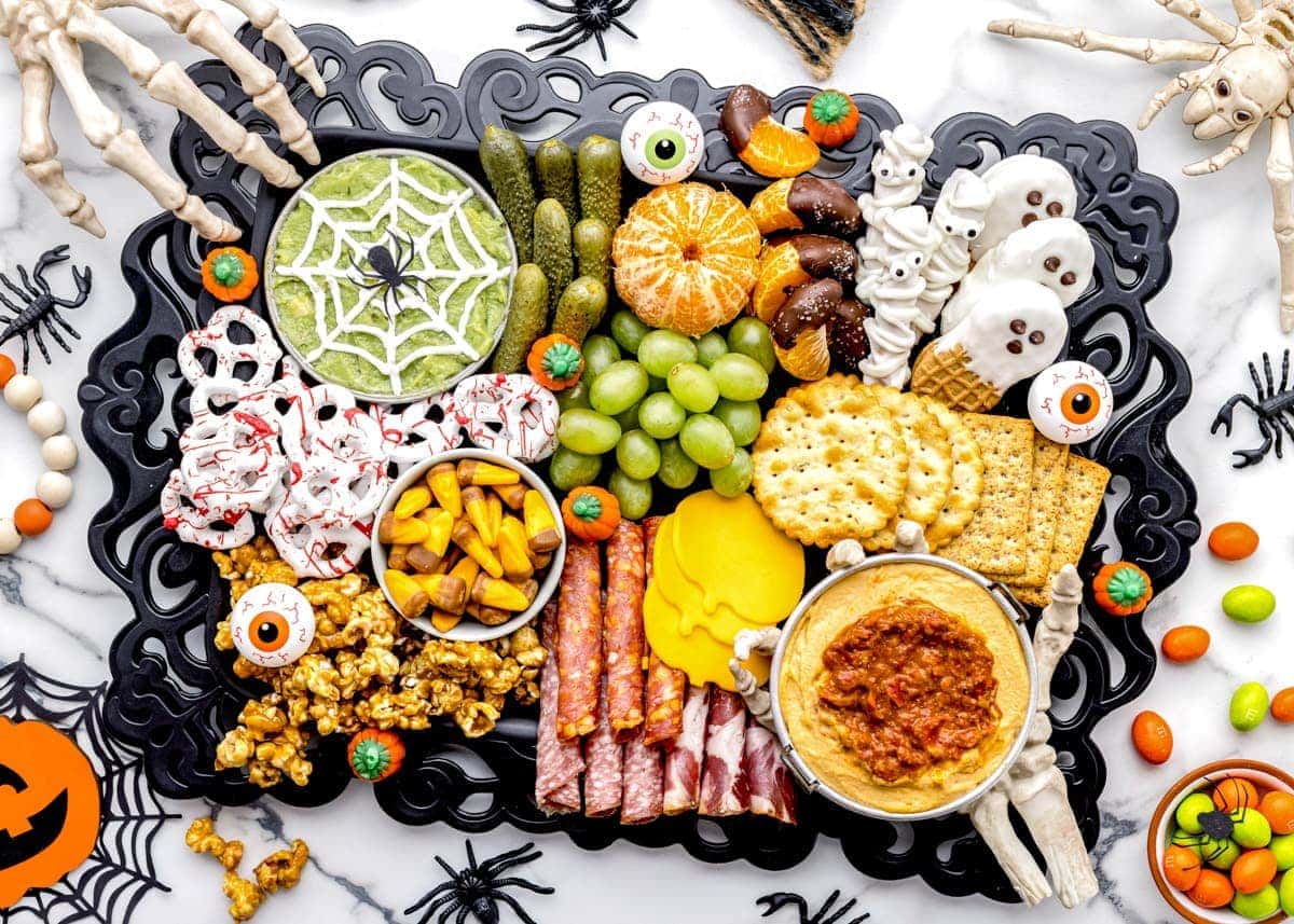 A halloween-themed charcuterie board filled with halloween snack and surrounded by halloween decorations 