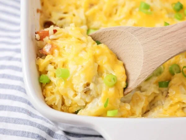 Cheesy hashbrown casserole baked in baking dish with scoop being spooned out.
