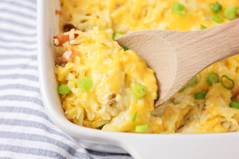 Cheesy hashbrown casserole baked in baking dish with scoop being spooned out.