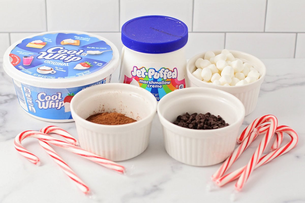 Cool whip, marshmallow fluff, and hot cocoa with toppings on a kitchen counter.