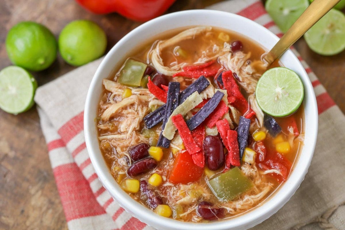 Bowl of chicken tortilla soup with colored tortilla strips on top and fresh lime on the side.