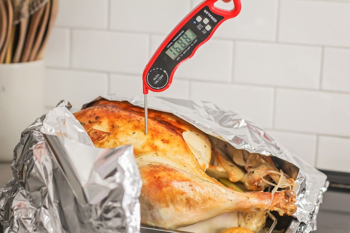 Roasted turkey with foil over it and a meat thermometer in it checking the temperature. 