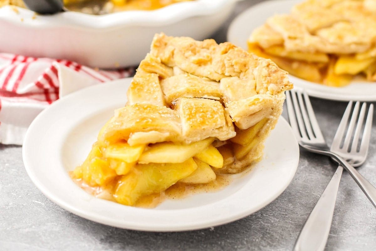 A slice of apple pie with two forks next to the plate. 