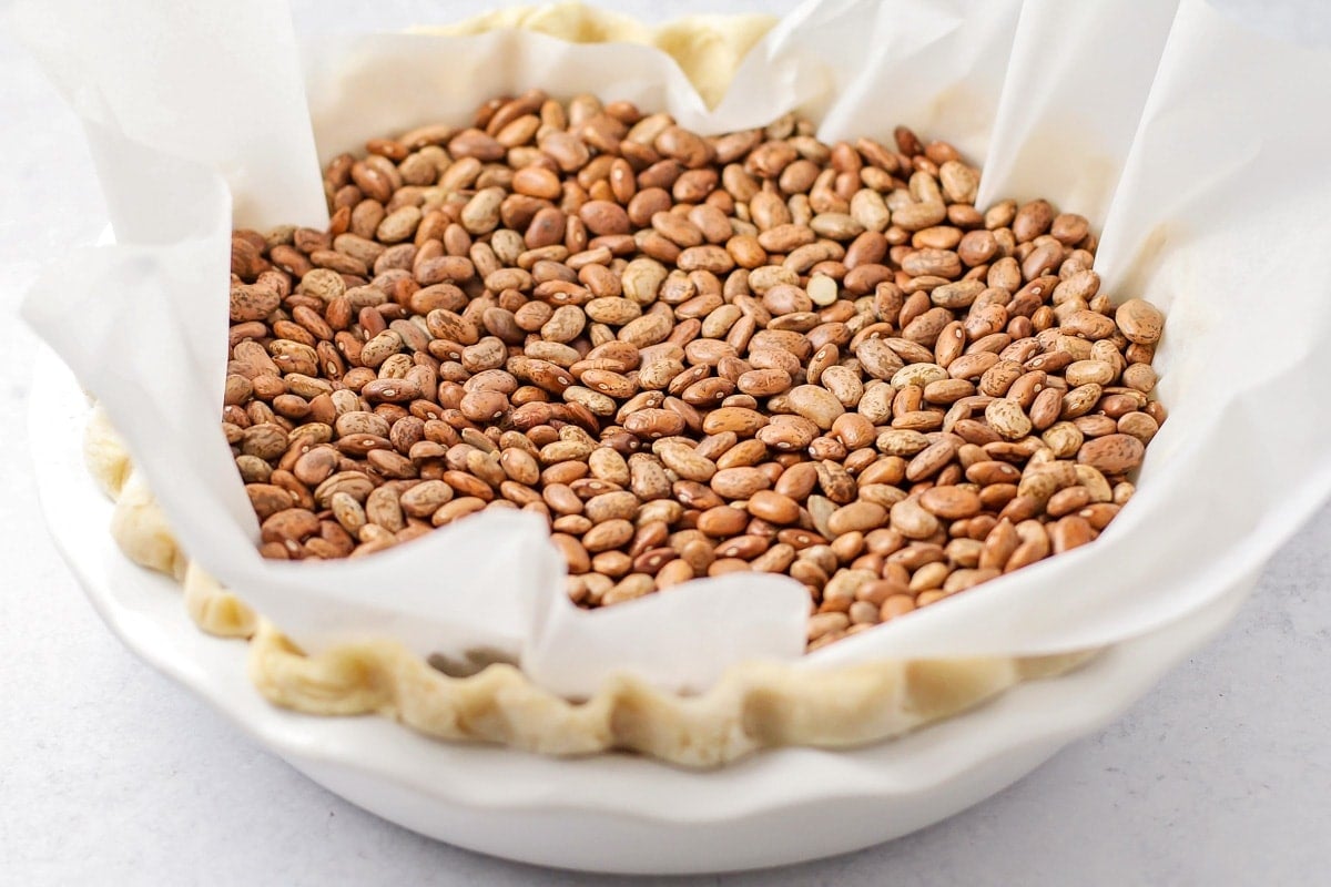 An unbaked pie with parchment paper and dried beans in the center of it. 