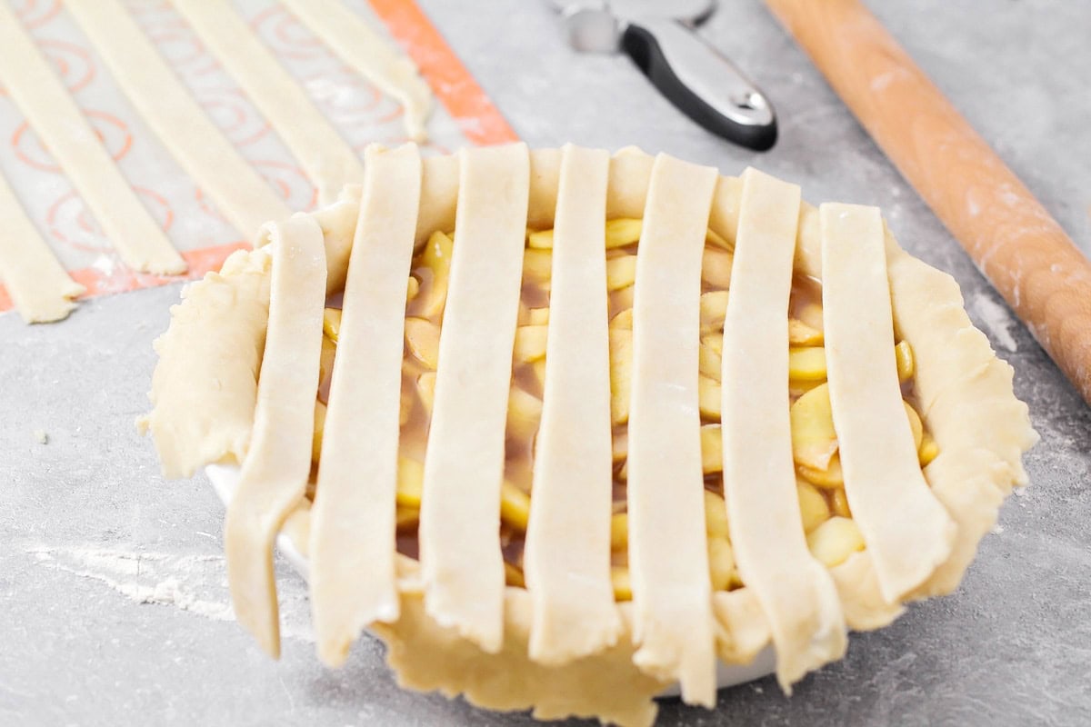 An uncooked apple pie with the beginning step of making a lattice pie crust. 