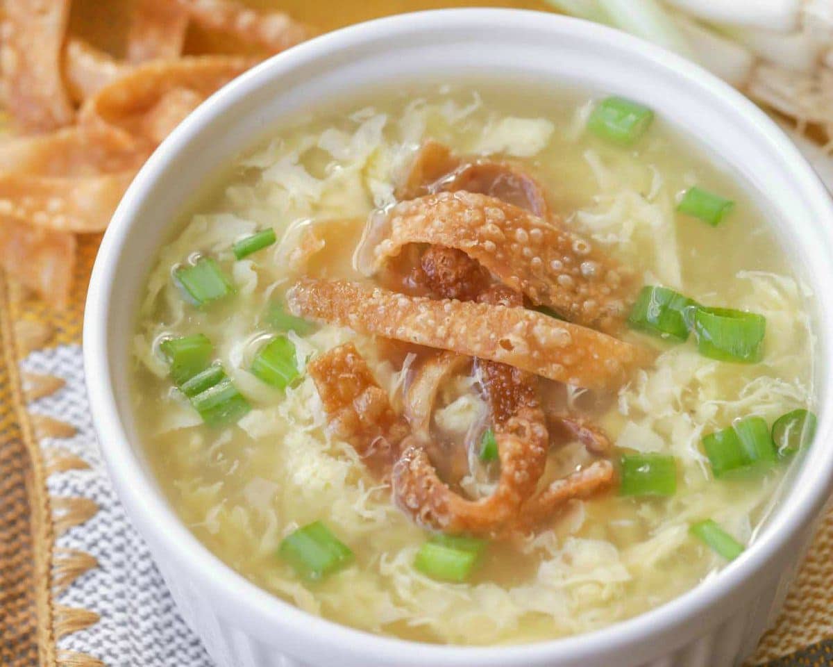 A bowl of egg drop soup topped with green onions and crispy wonton strips. 