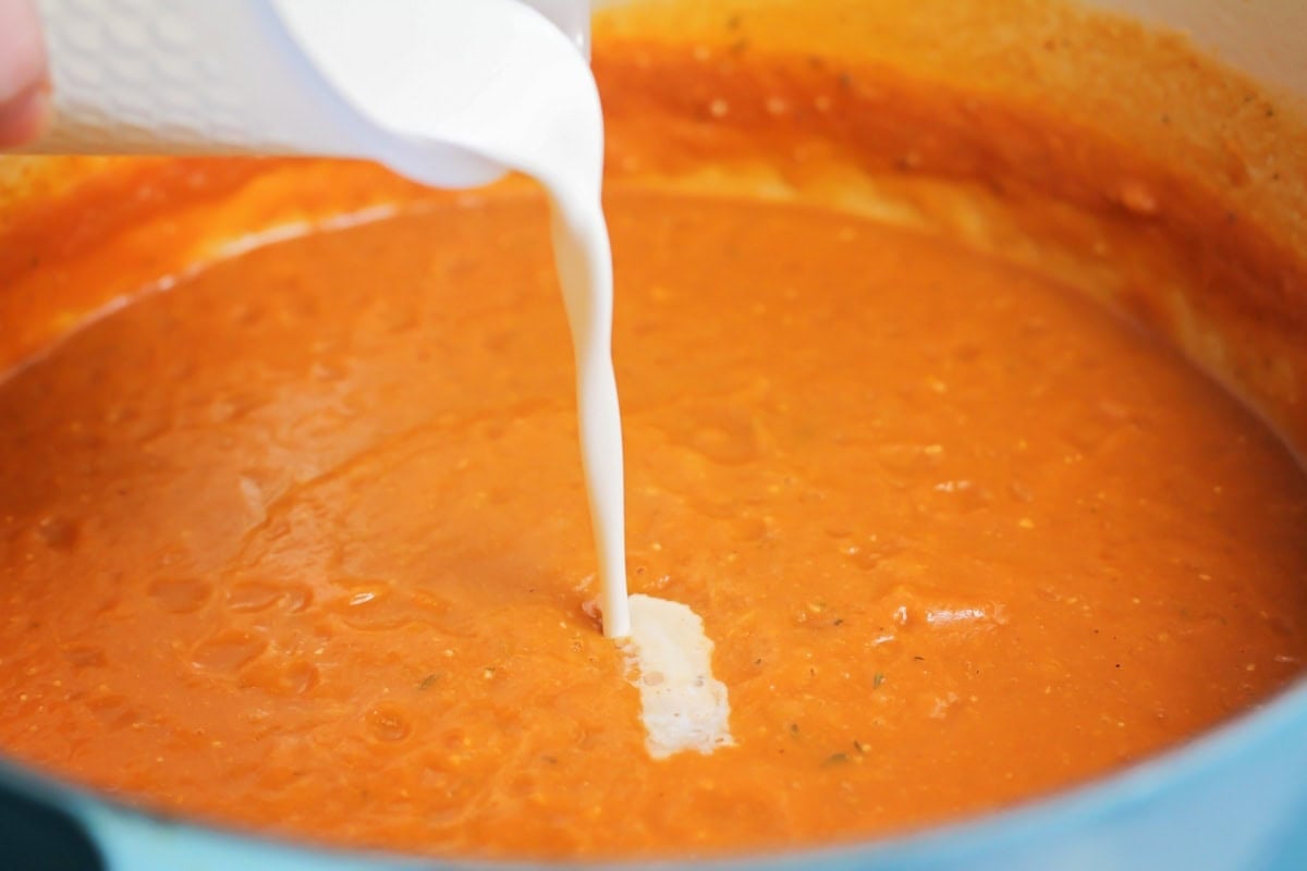 A pot of pumpkin soup with cream being poured into it