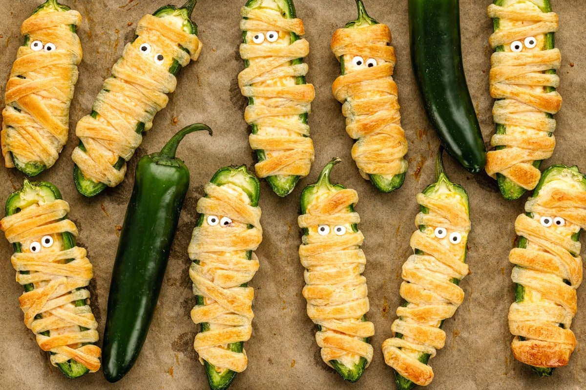 Jalapeño Popper Mummies on parchment lined pan with Jalapeños.